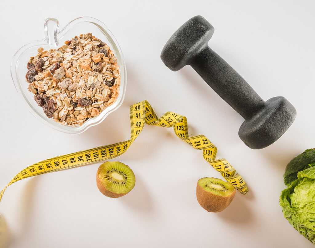 halved-kiwi-measuring-tape-oats-dumbbell-lettuce-white-surface 1