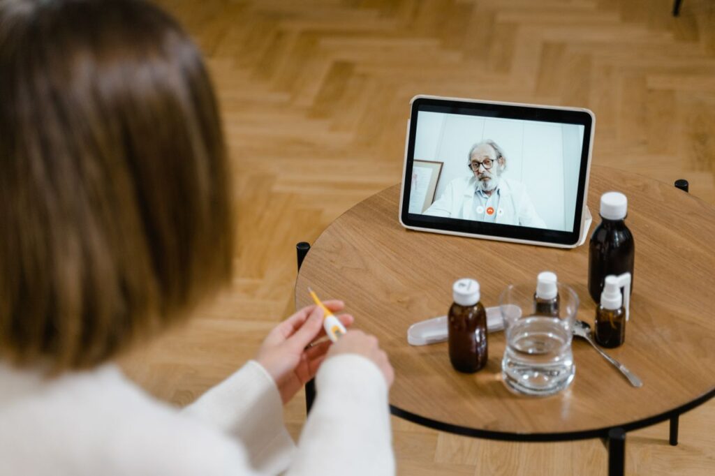 A doctor provides an online consultation via video call on a tablet, seen on a wooden table.