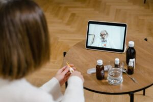 A doctor provides an online consultation via video call on a tablet, seen on a wooden table.